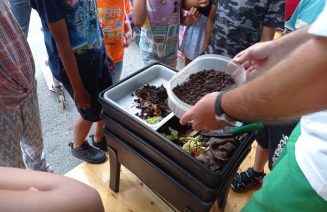 Fotografia de la darrera Festa de la Ciència, amb públic de diferents edats observant diferents estats de descomposició de restes orgàniques i una vermicompostadora.